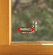 Close‑up of Andersen window glass etched with Andersen logo and the word "Tempered" circled in red to show it is tempered glass.