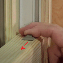 Close-up of a hand pushing the tilt-latch mechanism with a red arrow showing you move the mechanism toward the center of the window frame.